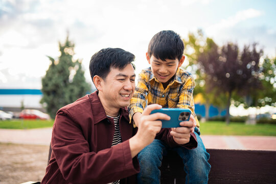 Father and son smiling while looking at a smartphone together