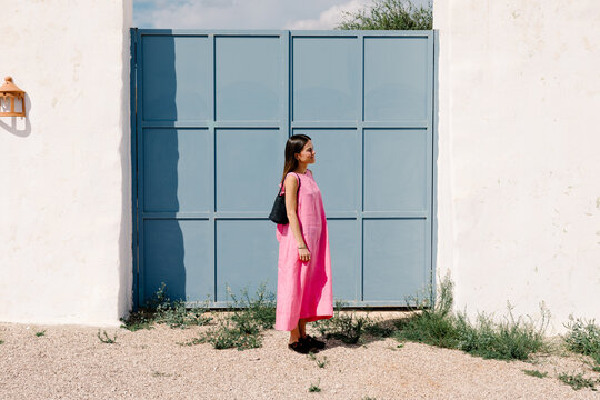 Female traveler in a pink dress, modeling in front of a blue gate