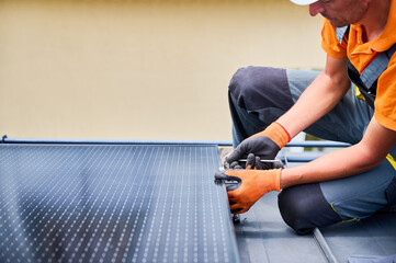 Worker building photovoltaic solar panel system on rooftop of house. Man engineer in gloves...