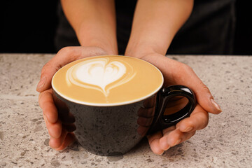 Coffee with a heart made of milk on a wooden table. Breakfast. Coffee with a painted heart and milk on a ceramic table in a coffee shop. Cafe, close-up photo.