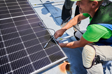 Workers building solar panel system on metal rooftop of house. Two men installers installing...