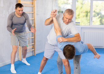 Elderly man and young man training self-defense techniques in studio..