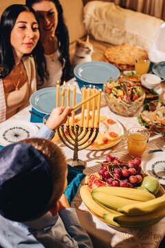 Little boy lighting a golden menorah at Hanukkah.