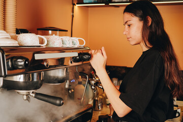The barista carefully prepares coffee in a cup, her skillful hands create a delicate heart-shaped latte, and she smiles warmly at the customer.