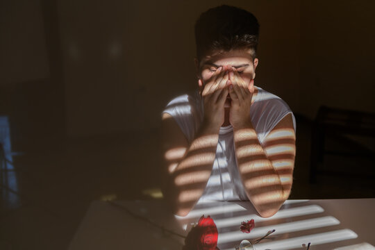 Non binary person covering face with hands, portrat in a shadows