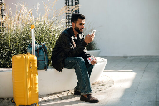 An Indian man waiting for train at station with a yellow suitcase.