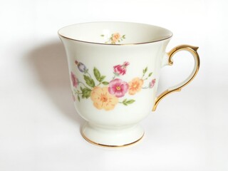  A porcelain tea cup with a delicate floral print and a gold handle, inspired by vintage English tea sets. The cup is centered on a white background.