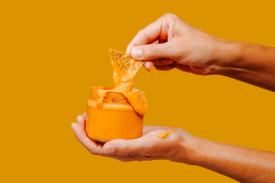 man dips  a tortilla chip in a jar of cheese sauce