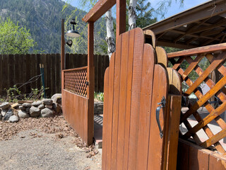 Beautiful view of an open wooden gate leading into a lush, green backyard on a sunny day