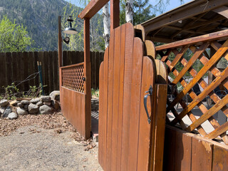 Beautiful view of an open wooden gate leading into a lush, green backyard on a sunny day