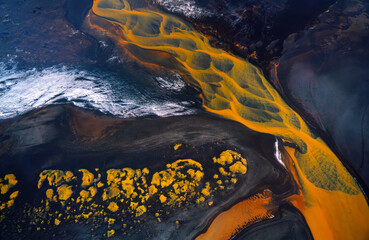 Aerial view of abstract orange river in Iceland with black sand