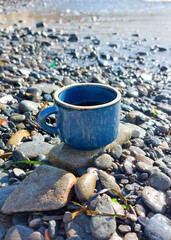 Blue coffee cup sitting on damp rocks by the seaside in the sunshine