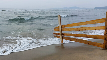Powerful waves eroding a weathered wooden fence on a deserted beach, capturing the relentless force of nature