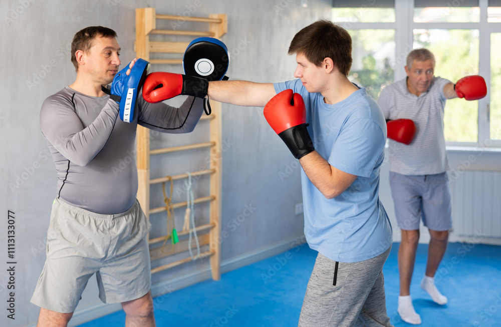 Wall mural Boxing training - young guy masters boxing strikes on the trainer punch mitts during training