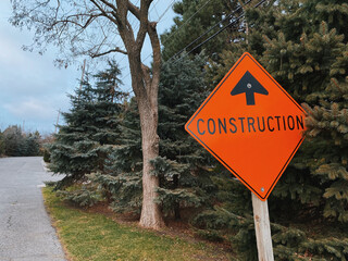 Orange Construction Sign Near Pine Trees on a Suburban Road