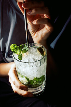 Hand stirring mojito cocktail with fresh mint