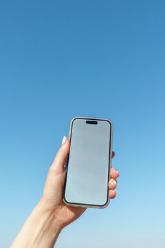 Hand Holding Smartphone with Blank Screen Against Clear Blue Sky