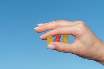 Hand Holding Three Gummy Bears Against Blue Sky