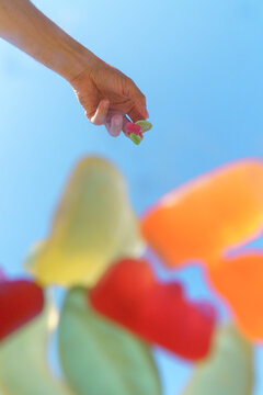 Hand holding colorful gummy candies with a bright blue sky background