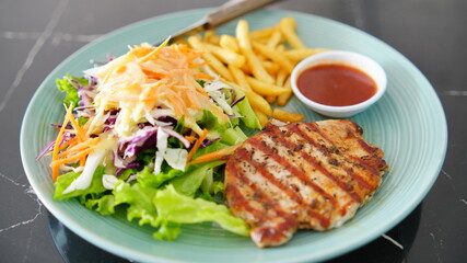 Colorful dish featuring a grilled chicken breast served with a fresh salad, golden fries and a side sauce on plate.