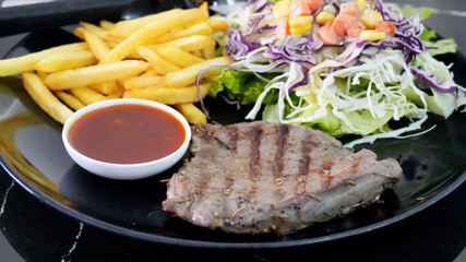 Colorful dish featuring a grilled beef breast served with a fresh salad, golden fries and a side sauce on plate.