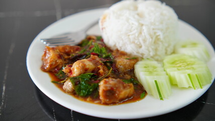 Plate of spicy Thai basil chicken stir-fry served with steamed white rice and fresh cucumber slices.