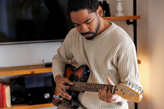 Serious young man practicing electric guitar at home