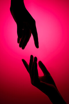 Two reaching hands silhouettes against gradient pink background. 