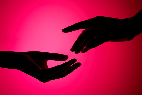 Two reaching hands silhouettes against gradient pink background. 