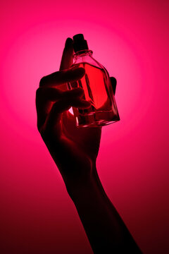 Hand holding a glass fragrance bottle on a vibrant pink background.
