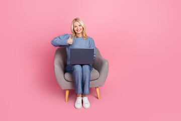 Full length photo of lovely pensioner lady sit armchair netbook thumb up dressed blue knitted garment isolated on pink color background