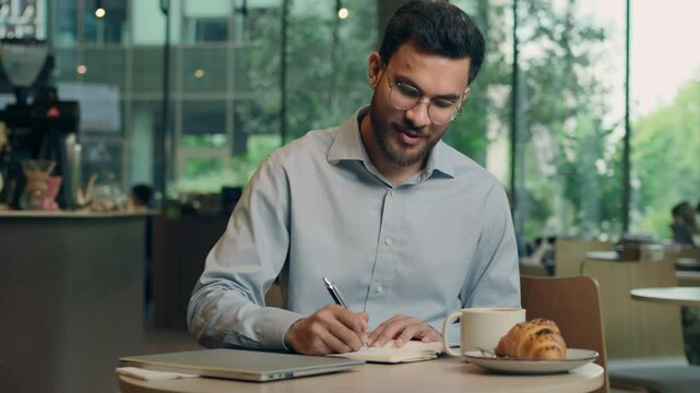Indian businessman Arabian man guy male business entrepreneur employee student writing in notebook studying in cafe customer write notes freelancer work learn tasks answer mobile call message reading