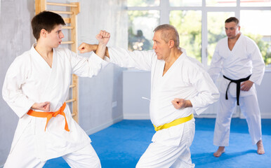 Elderly man and young man in kimono practicing karate techniques in gym