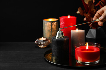Woman with beautiful burning candles and decor on black table, closeup. Space for text