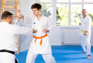Concentrated young guy in kimono honing punching techniques during kumite with male opponent at...