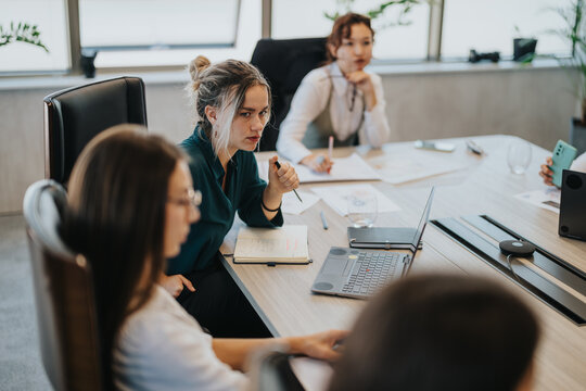 A group of multicultural business people engaged in a focused discussion during a team meeting in a modern office environment. Laptops and documents are on the table, fostering collaboration.