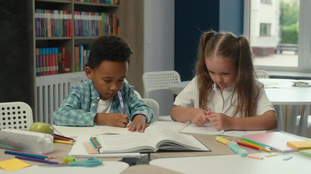 Multiethnic little kids classmates African boy Caucasian girl daughter son elementary school education pupils students children study learn write at desk together schoolgirl schoolboy lesson homework