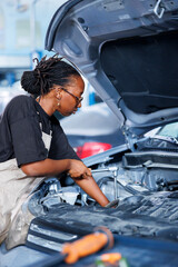 BIPOC woman in car service using professional mechanical tool to repair broken emission system....