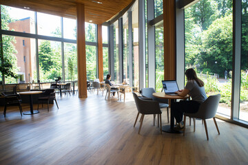 Fototapeta premium student studying in bright, modern cafe with large windows and greenery. inviting atmosphere encourages focus and creativity
