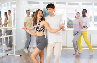 Happy young woman dressed in sportswear with man dancing bachata during group dance lesson in modern ballroom dance class