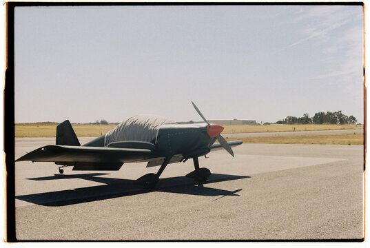Small airplane parked on a runway,covered with a protective tarp. Film