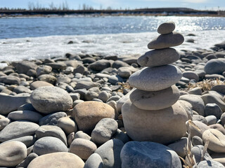 A carefully balanced stack of smooth stones rises gracefully on a pebble-strewn shore, with the...
