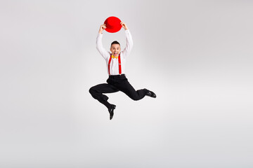 Dynamic young man leaping joyfully with a vibrant red hat in a stylish dance pose against a white...