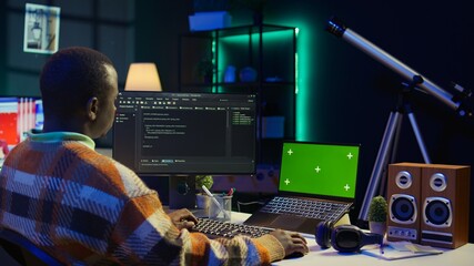 Black web developer handling database servers for safety with green screen, writing code on terminal window next to isolated chroma key. Programming language for machine learning. Camera B.