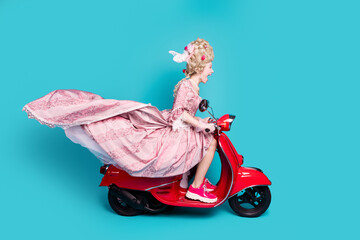 Photo of positive charming lady princess driving fast moped scooter isolated on blue color background © deagreez
