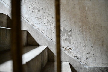 A stairwell in a nearly empty old apartment catches scattered sunlight, illuminating terrazzo steps and a peeling white wall, reflecting the passage of time and urban change.