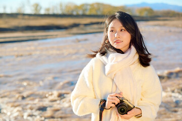 Asian female photographer holding camera outdoors in late autumn