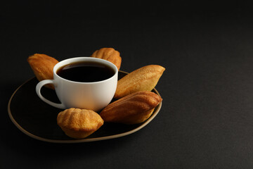 Madeleine cakes and cup of coffee on black background, space for text
