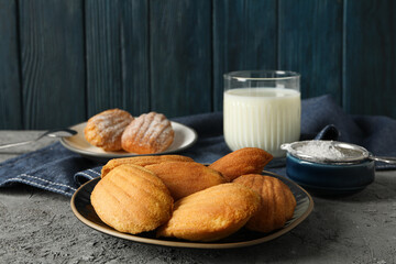 Madeleine cakes, glass of milk, flour and towel on blue wooden background
