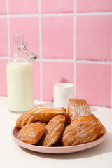 Madeleine cakes, milk jug and bottle of milk on pink background